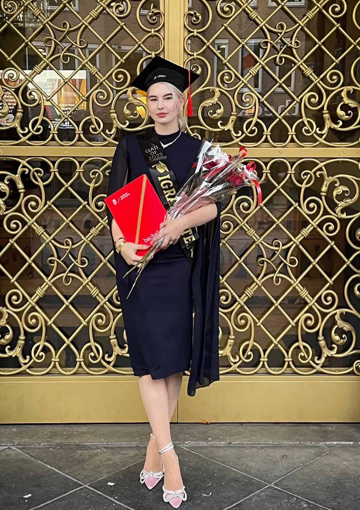 graduate wearing midi dress under cap holding flowers at graduation ceremony