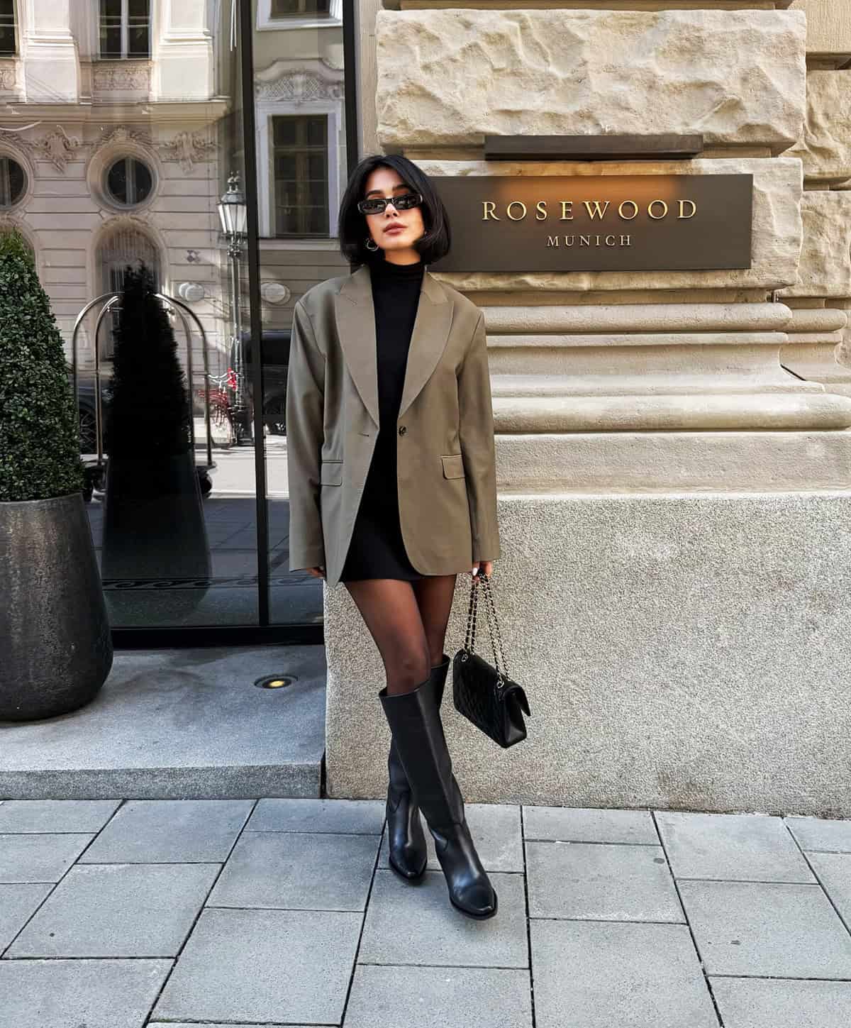 tailored blazer layered over a black mini dress with knee high boots for winter cocktail outfit