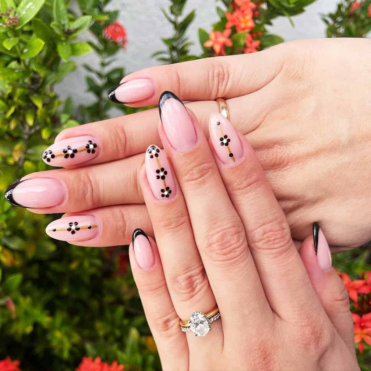 nude pink almond nails with thin black French tips and delicate floral dot details, classy black baddie nails