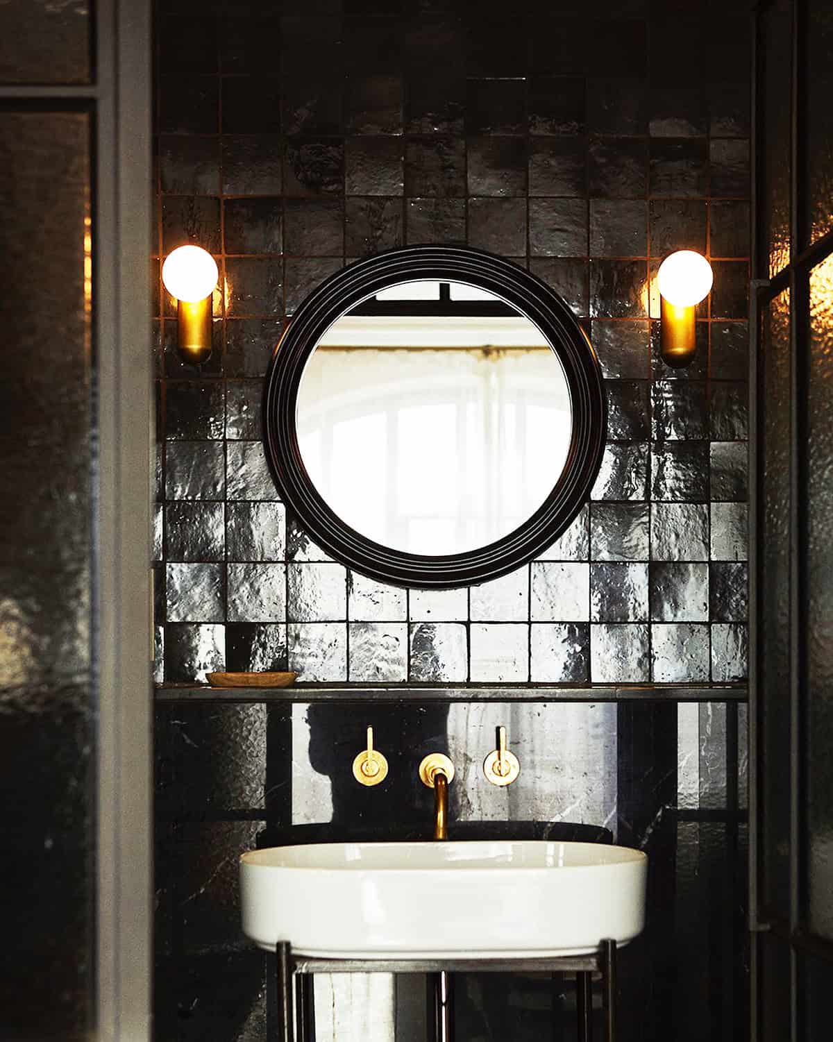 moody black tiled bathroom with warm sconces and reflective surfaces black bathroom ideas