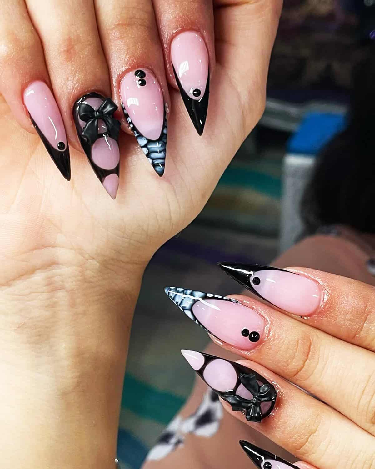 nude pink stiletto nails with black tips, 3D bow details, and dot accents, soft glam black baddie nails