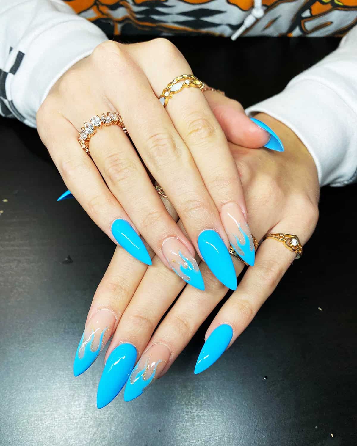 long blue stiletto nails with sheer accent nails and gold glitter flame details fire nails