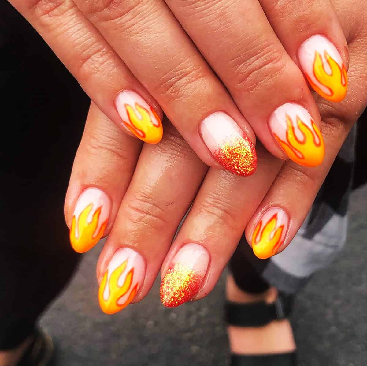 short white almond nails with orange yellow cartoon flames and red gold glitter accent nail fire nails