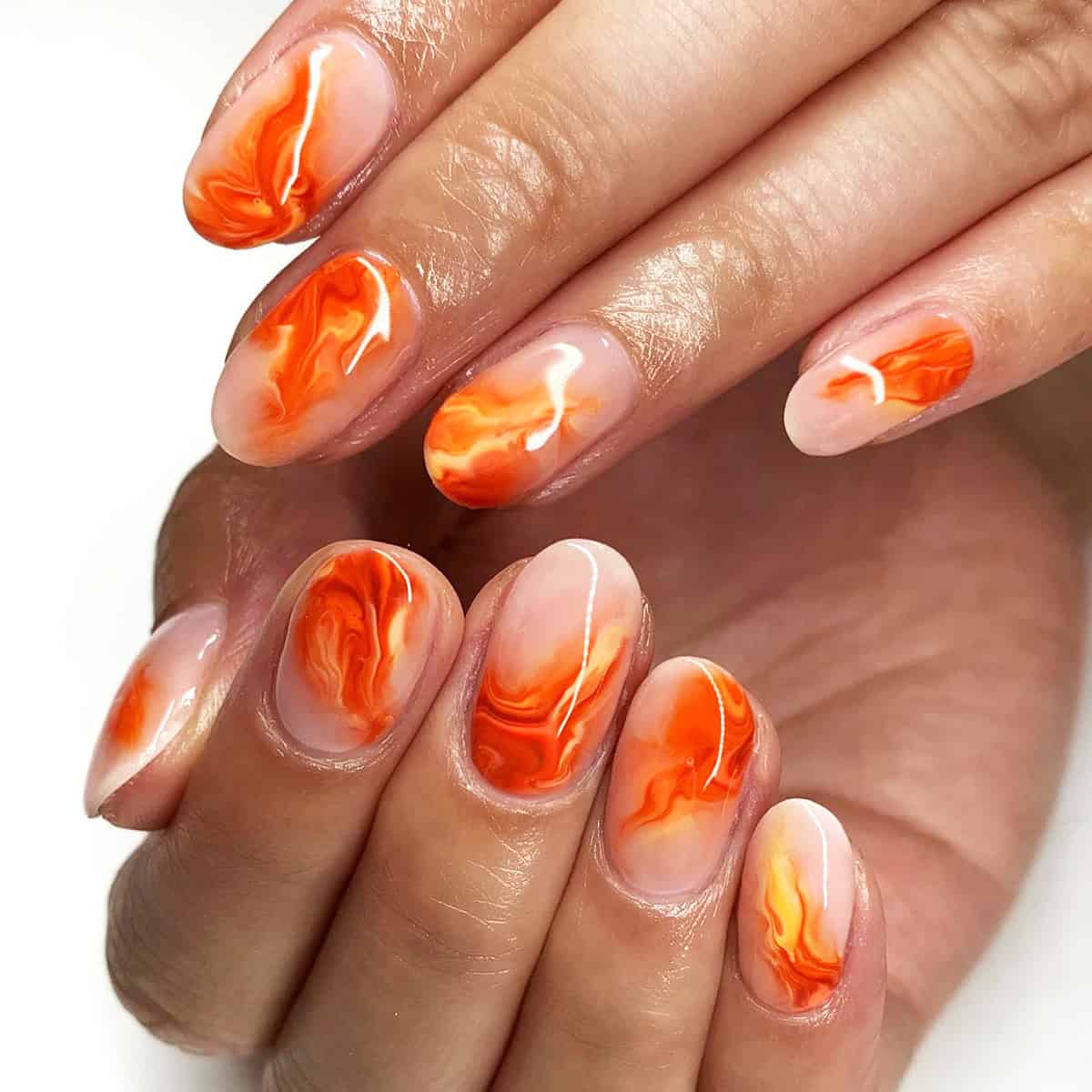 short almond nails with swirled orange marble flame nail art on sheer base fire nails