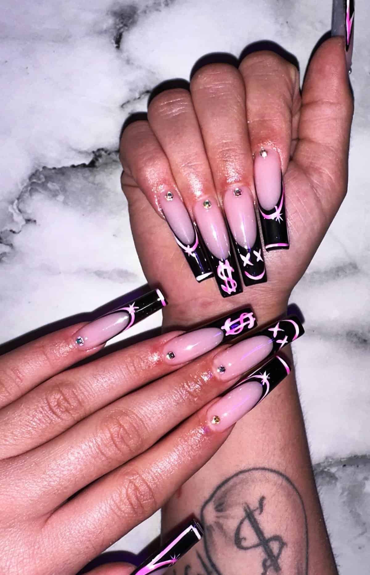long square nails with pink base, black tips, and graphic star and dollar sign designs, playful black baddie nails
