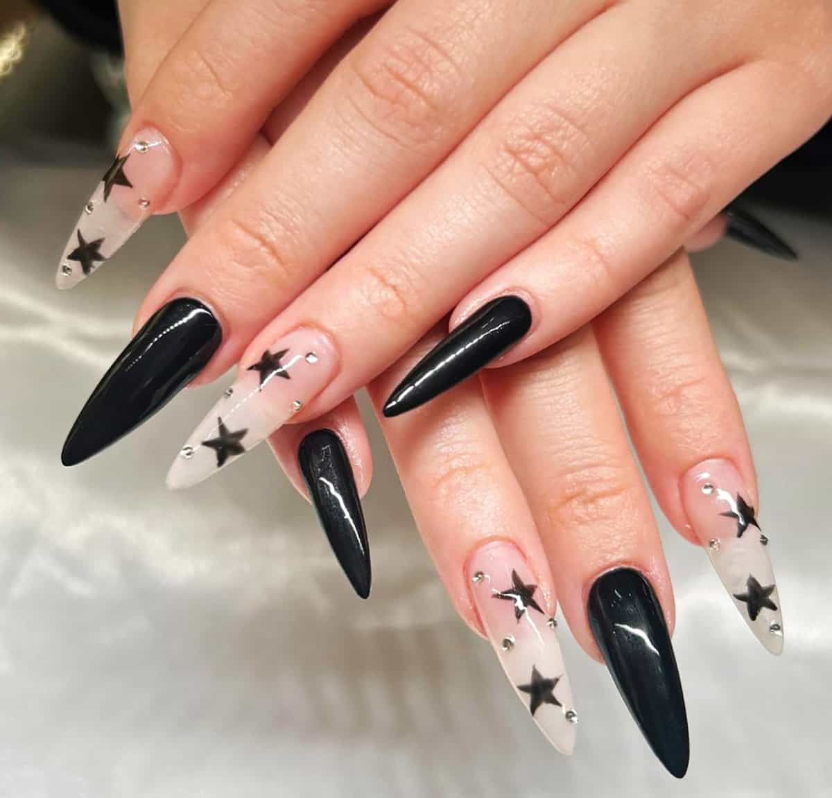 black stiletto nails mixed with clear nails featuring star designs and rhinestones, Y2K black baddie nails