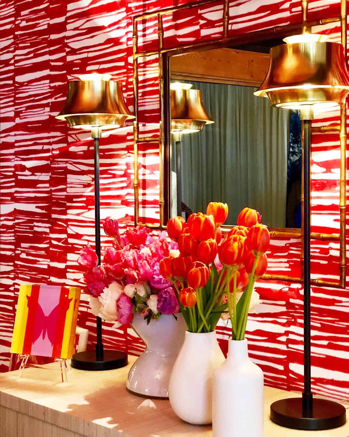 bold red and white abstract brushstroke wallpaper with brass lamps and fresh flowers on a vanity pink wallpaper ideas home decor