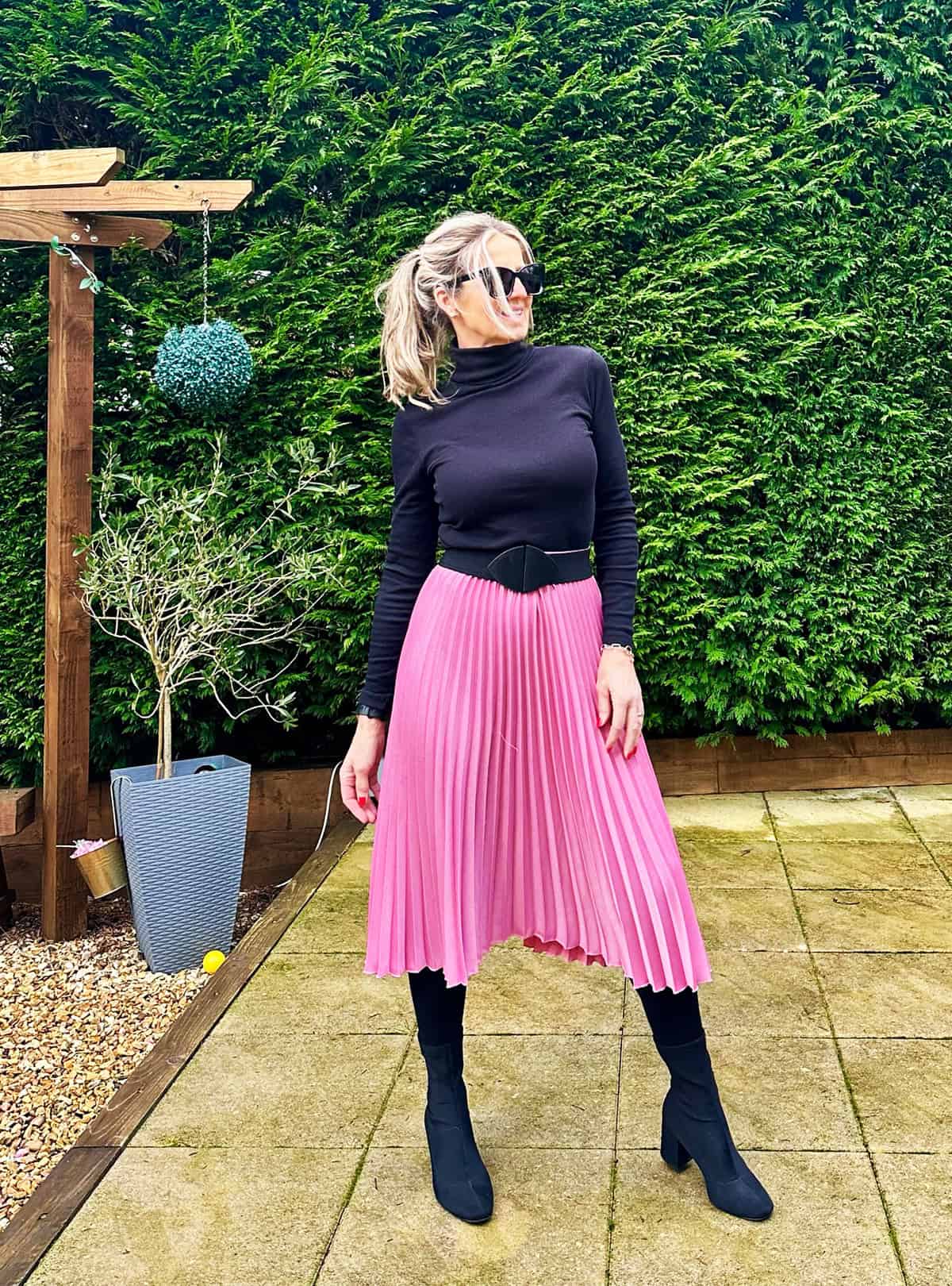 black turtleneck with pink pleated midi skirt, black corset belt and knee-high boots for office attire for women over 40