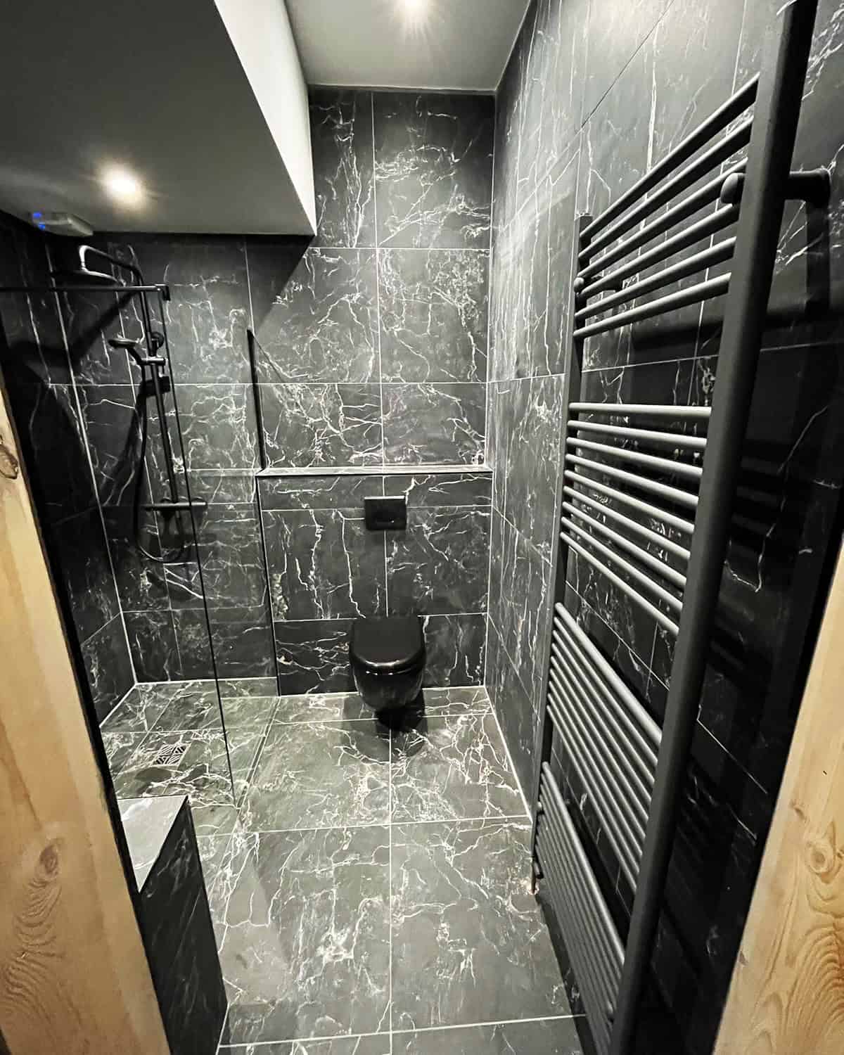 enclosed black marble  tile bathroom with strong lighting creating a seamless look, black bathroom ideas