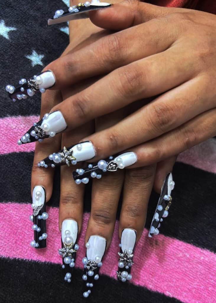 long coffin nails with black and white base covered in pearls and metallic charms, statement black baddie nails