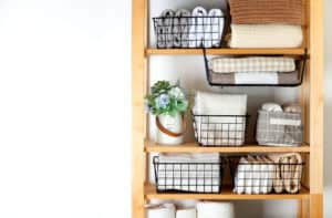Vertical tidying up storage. Neatly folded bed sheets in the metal black baskets for wardrobe. Nordic style.