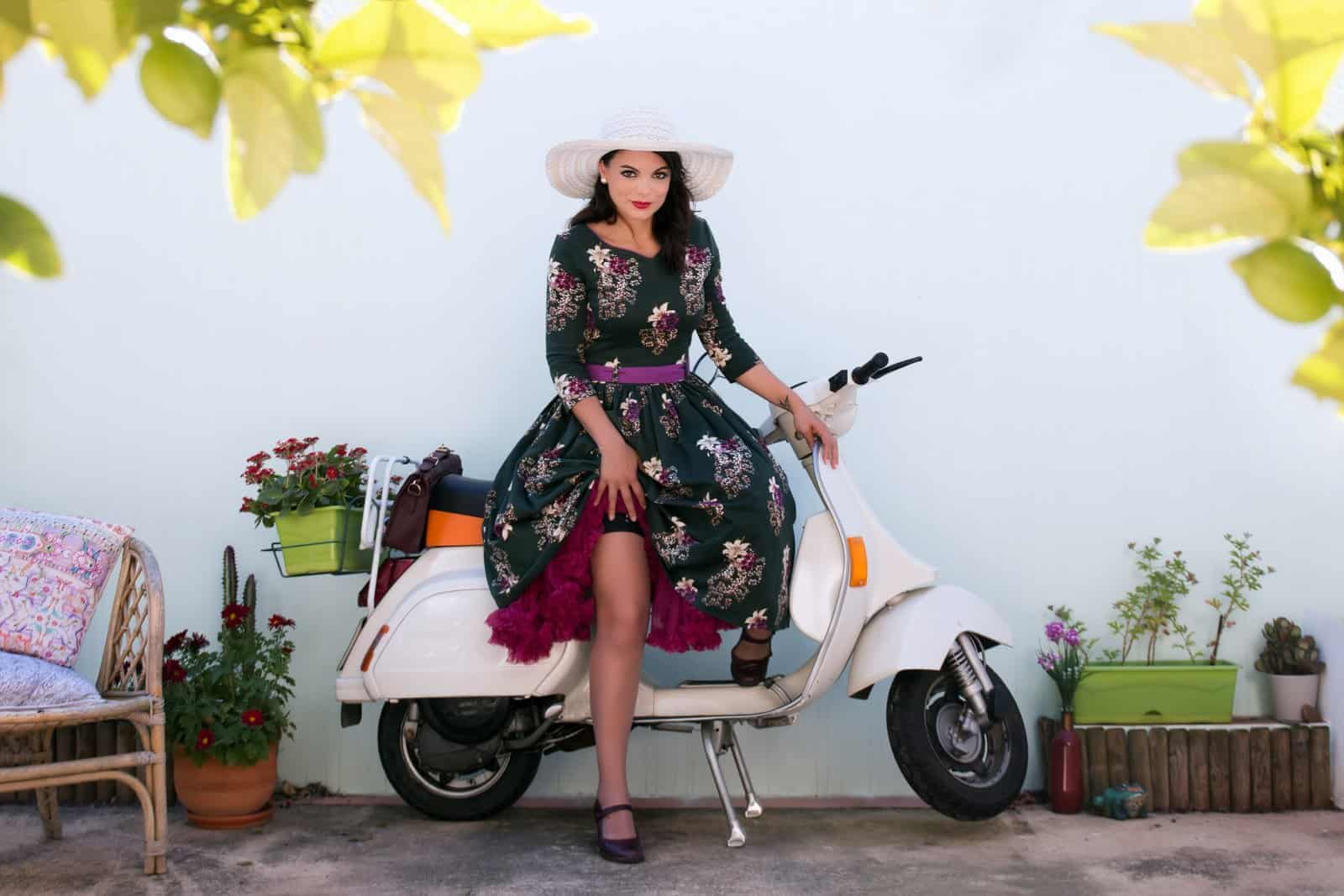 Vintage girl with beautiful floral dress next to a classic motorcycle.
