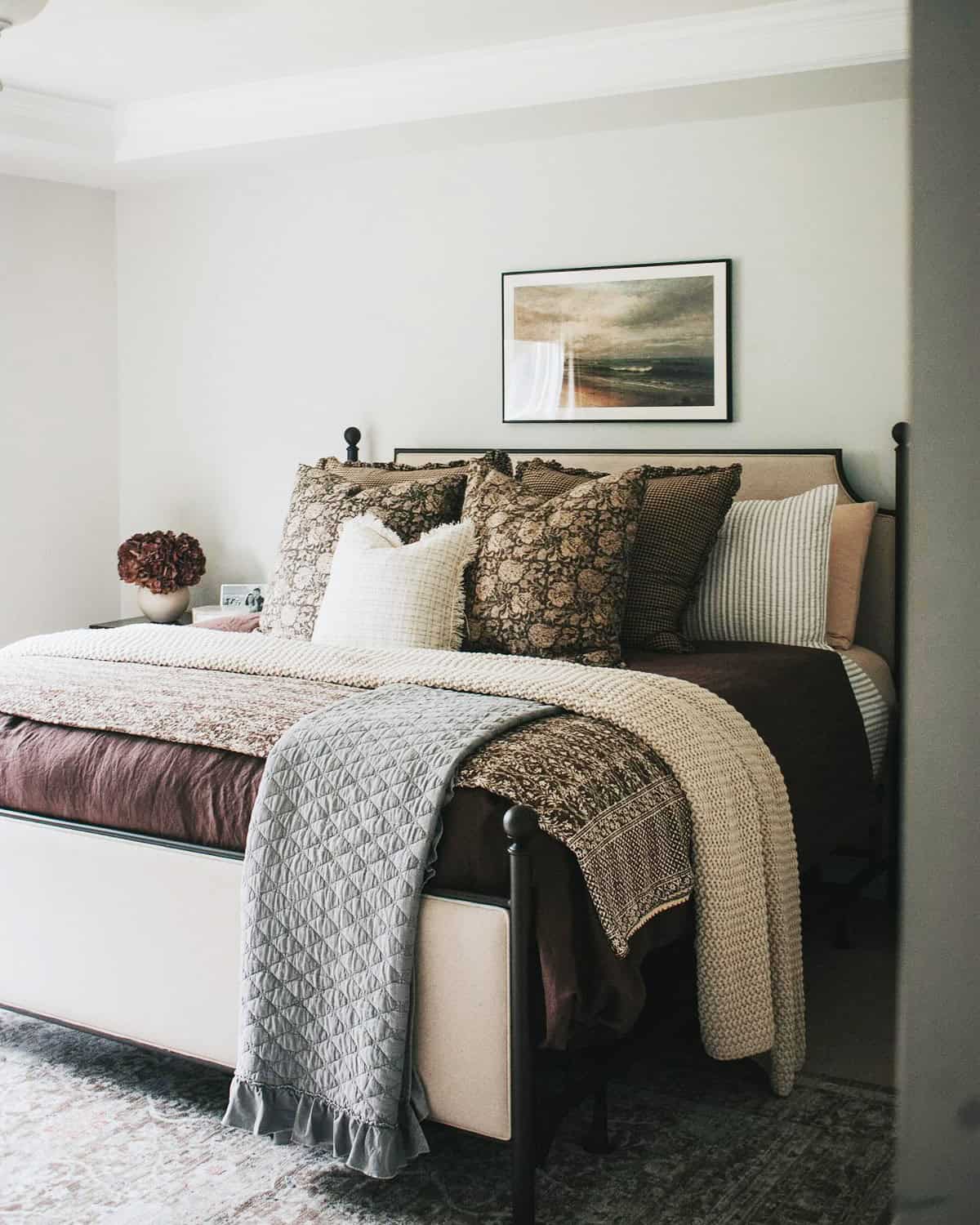 layered neutral bedding with quilt and knit throw, warm brown tones, cozy pillows cottagecore bedroom insp