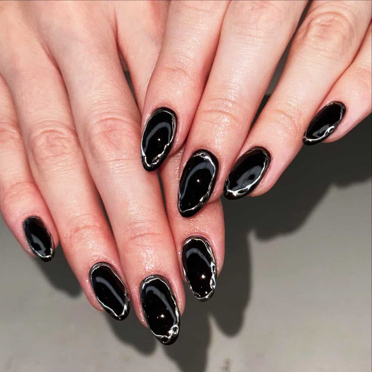 short almond nails with glossy black base and silver chrome outline black chrome nails